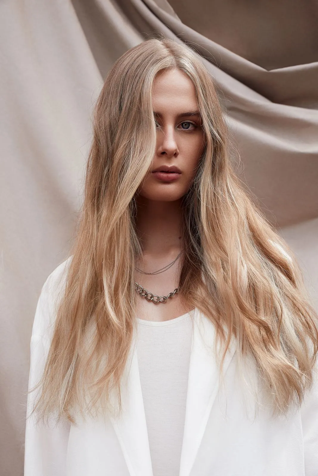 Model mit langen, warmen Blonde-Wellen vor einem Stoffhintergrund